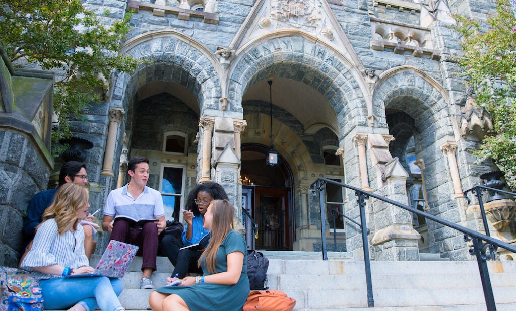 A group of students sitting together on the steps of a building on the Georgetown campus.