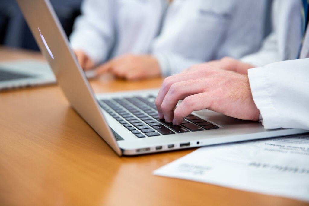 View of two medical students sitting around a table with their laptops open. They are wearing white coats.