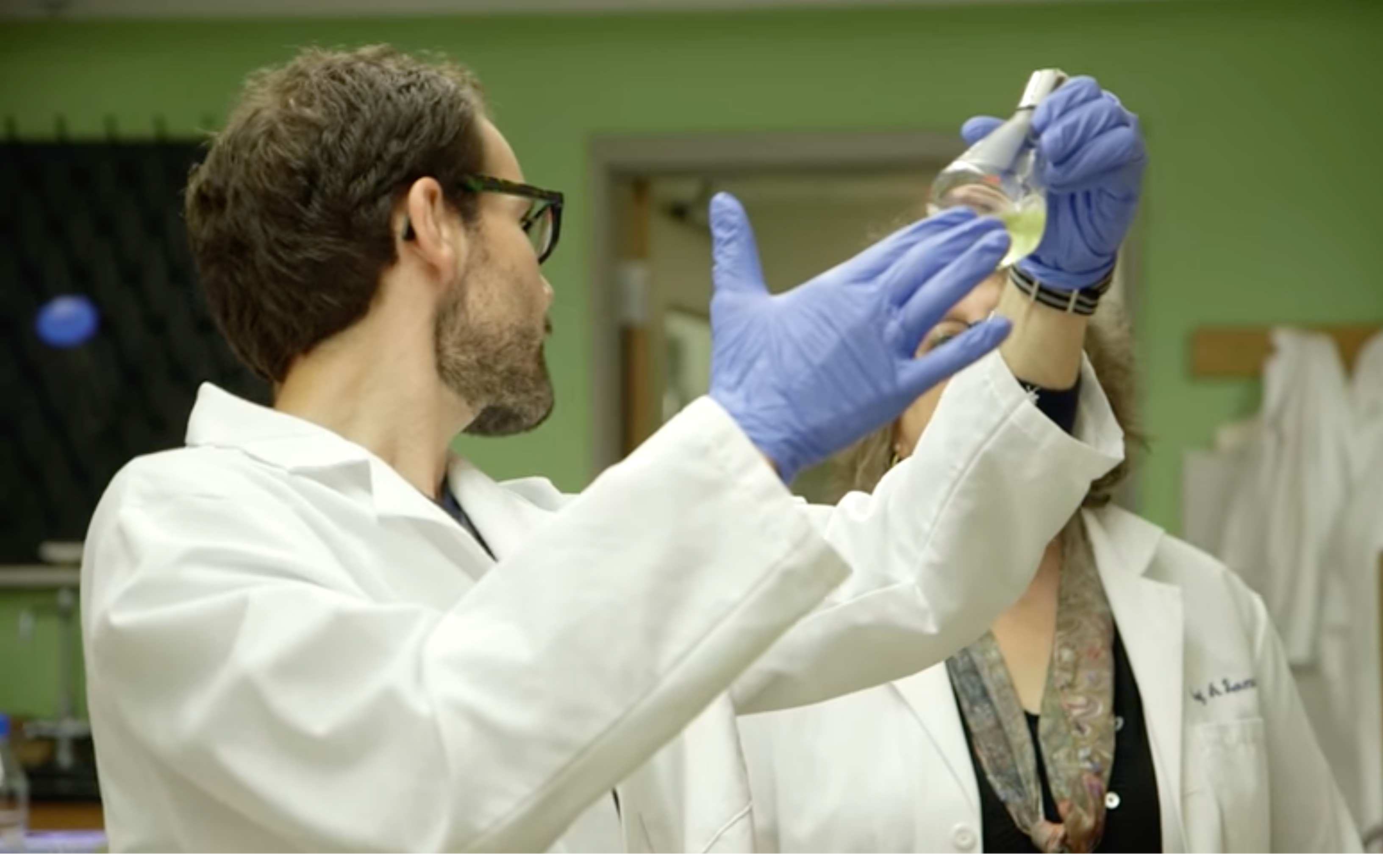Man in a lab coat and gloves holding glassware